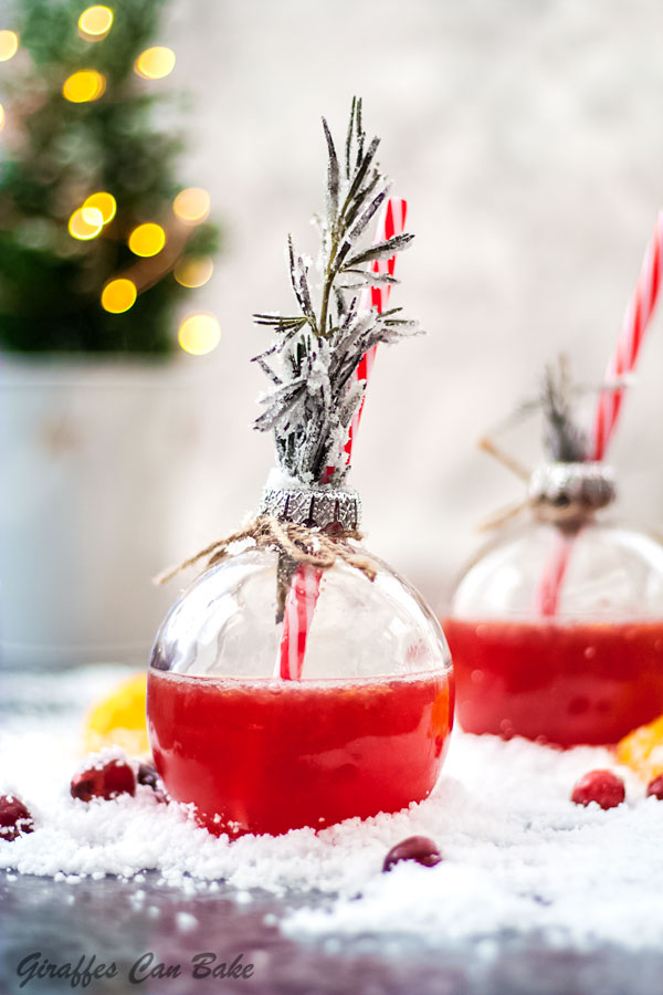 This Holiday Gin and Tonic is full of the festive flavours of cranberry and clementine - one bauble glass in focus, with red gin and tonic and rosemary