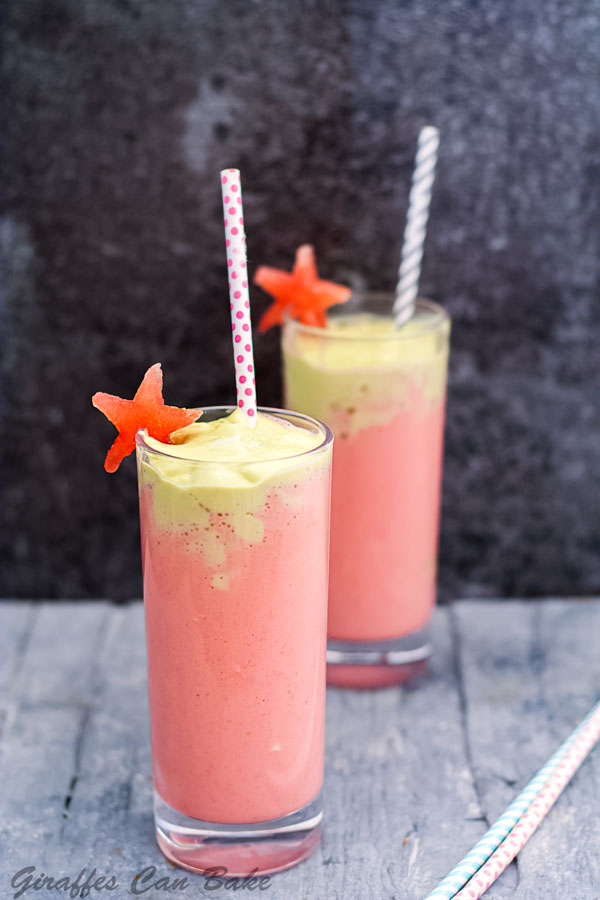One glass of citrus smoothie with pink and green layer in front with straw, one in background with straw